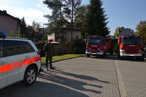 policjant i dwóch żołnierzy WCR, obok zaparkowane pojazdy straży pożarnej