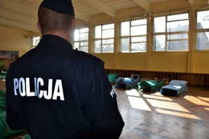 sala gimnastyczna, policjant odwrócony tyłem, w tle osoby leżące na leżakach