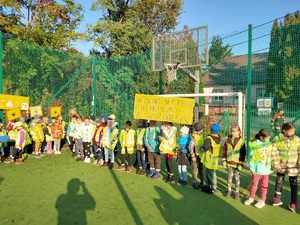 dzieci ubrane w kamizelki odblaskowe stoją na boisku szkolnym z transparentami w ręku