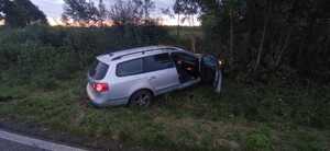 samochód osobowy w srebrnym kolorze z otwartymi drzwiami przednimi od strony pasażera znajdujacy się w rowie przy zalesionym terenie