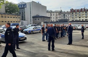 Parking przy Komendzie Miejskiej Policji w Krakowie, rezerwiści stoją w dwuszeregu, obok policjanci, w tle widac radiowozy