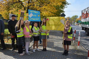 dzieci z transparentami w rejonie przejścia dla pieszych ubrane w kamizelki odblaskowe