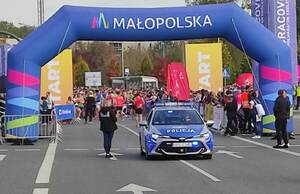 uczestnicy biegu stojący przed linia startu biegu. Na pierwszym planie widać policyjny radiowóz