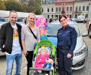 wspólne zdjęcie Amelki w wózku, jej rodziców oraz policjantki, dziewczynka ma w wózku policyjną maskotkę