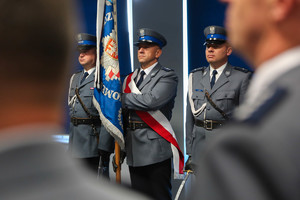 poczet sztandarowy - trzech policjantów ze sztandarem zza ramienia policjanta
