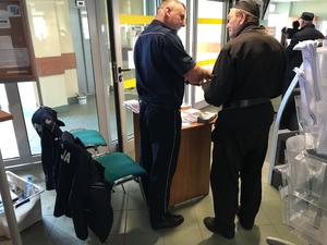 policjant prowadzący rozmowę ze starszym mężczyzną ubranym na czarno przed stanowiskiem przeznaczonym dla seniorów