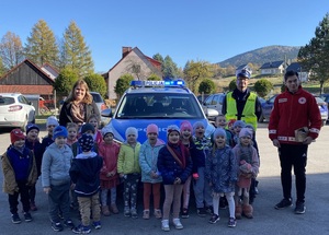 dzieci spozujace do zdjęcia z policjantem panią nauczyciel na tle radiowozu