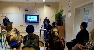 siedzący uczestnicy debaty oraz  dwóch stojących policjantów którzy przedstawiają temat spotkania