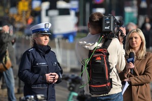 Policjantka ruchu drogowego udziela wywiadu na żywo dziennikarce stacji TVP3 Kraków. Między nimi stoi  opertor z kamerą. W tle ruch uliczny