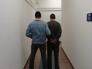 policjant nieumundurowany prowadzi zatrzymanego, który ma ręce spięte kajdankami