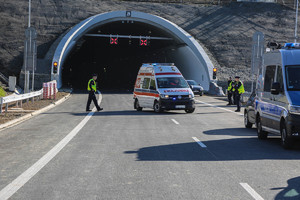 karetka pogotowia wyjeżdżająca z tunelu. Przed tunelem stoją policjanci i radiwozy policyjne