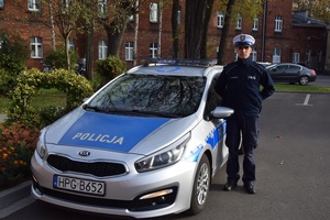 sierżant sztabowy Kamil Jaśkiewicz stoi przy radiowozie na terenie dziedzińca Komendy Miejskiej Policji w Krakowie.JPG