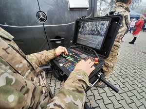 chłopiec w kamizelce odblaskowej siedzący na motocyklu policyjnym, obok policjant stojący tyłem, w tle grupa osób