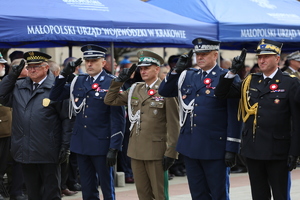 Delegacja służb mundurowych salutuje przed grobem po złożeniu wiązanki