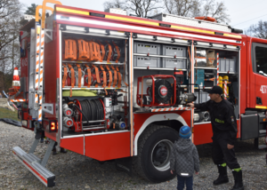 Strażak omawia uczestnikowi akcji strażacki sprzęt znajdujący się na stanie wozu strażackiego