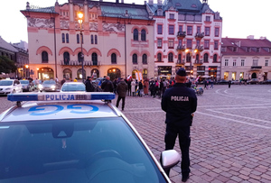 policjant przy radiowozie na placu Szczepańskim w tle kamienica i grupa ludzi