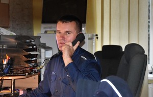 Oficer dyżurny Komendy Powiatowej Policji w Bochni trzymający w ręku słuchawkę telefonu
