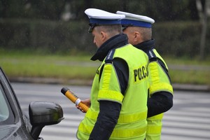 Dwóch policjantów ruchu drogowego badają trzeźwość zatrzymanego do kontroli kierowcy przy pomocy elektronicznego urządzenia