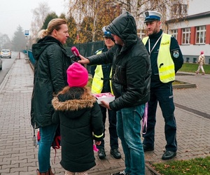 dziennikarz radiowy rozmawia z kobietą i dzieckiem. obok stoją policjanci, w tle budynek szkoły