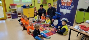 przedszkolaki wraz z policjantami siedzą na dywanie podczas omawiania zasad używania elementów odblaskowych