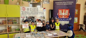 dzieci ubrane w elementy mudruru policyjnego przed plakatem Dzień z Policjntem na pamiątkowej fotografii