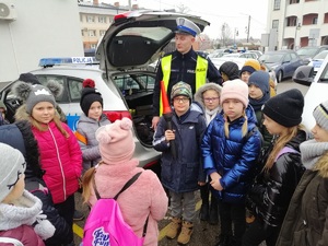 dzieci przy radiowozie oznakowanym ruchu drogowego, policjant umundurowany, dzieci zebrane obok niego trzymją tarczę i latarkę