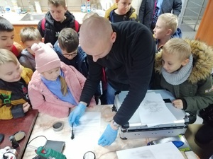 technik kryminalistyki demontruje jak ściąg się odciski palców, dzieci zebrane wokół niego