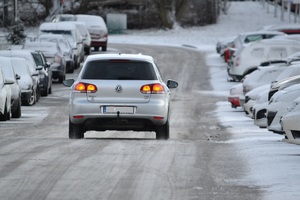 samochód jadący po jezdni pokrytej śniegiem. Po bokach zaparkowane inne pojazdy