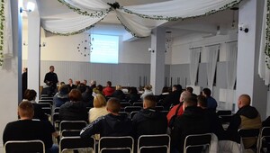 uczestnicy debaty siedzący tyłem, w tle przodem do nich stojący dzielnicowy a za nim widoczna wyświetlona prezentacja