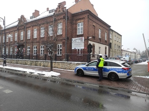 2.	Policjant i policjantka ruchu drogowego stoją przy oznakowanym radiowozie. Policjanci zabezpieczają wjazd do szkoły. W tle budynek szkoły. Pogoda zimowa, na chodnikach widać śnieg.