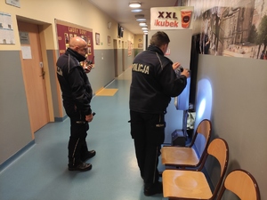 9.	Dwaj policjanci z latarkami sprawdzają korytarz, w poszukiwaniu niebezpiecznego urządzenia. Policjanci  sprawdzają stojący na korytarzu automat do kawy.