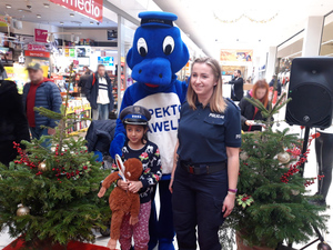 dziewczynka w policyjnej czapce z rarczą do zatrzymywania pojazdów i maskotką stoi obok policjantki i maskotki krakowskiej policji Inspektora Wawelka, w tle wnętrze marketu i ludzie