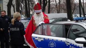 Święty Mikołaj w towarzystwie policjantów wysiada z ich radiowozu pod jednym ze szpitali