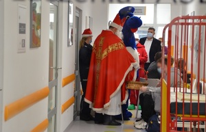 Na szpitalnym korytarzu Mikołaj z inspektorem Wawelkiem i policjantami wręczają dzieciom prezenty.