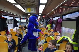 dzieci siedzące na siedzeniach w pociągu witają się z maskotką krakowskiej Policji, Inspektorem Wawelkiem