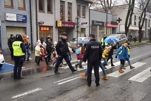 dzieci przechodzą przez przejście dla pieszych w towarzystwie policjantów i opiekunów