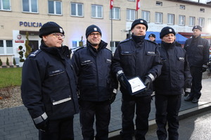 Policjanci stojący przed budynkiem posterunku trzymający w rękach dokumenty