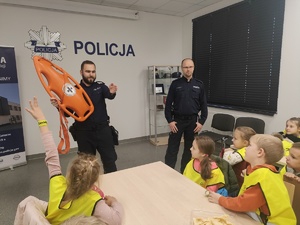 Pierwszaki z Piotrowic odwiedziły policjantów policjant prezentuje dzieciom bojkę ratowniczą na stołach sprzęt policyjny