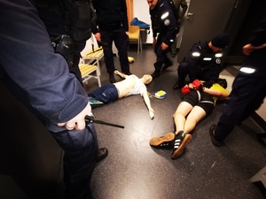 Manekin z podłączonym defibrylatorem, obok obezwładniony mężczyzna