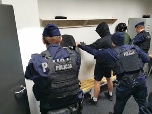 Policjanci sprawdzają mężczyzn w kapturach odwróconych do ściany
