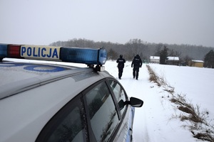 policjanci umundurowani na zasypanej drodze w tle na pierwszym kadrze radiowóz oznakowany