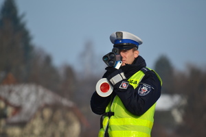 Policjant ruchu drogowego mierzy prędkość pojazdów ręcznym miernikiem.