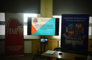 Banery z logo Komendy Powiatowej Policji w Bochni oraz II Liceum Ogólnokształcącego w Bochni oraz wyświetlona informacja o debacie społecznej i jej temat