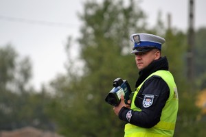 Policjant ruchu drogowego nadzoruje ruch, trzyma w ręku ręczny miernik prędkości