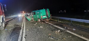 Uszkodzony w zdarzeniu drogowym samochód koloru zielonego. Na drodze liczne elementy plastikowe. Po lewej stronie fragment wozu strażackiego