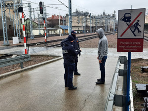 funkcjonariusze legitymują mężczyzna ubranego w szarą bluzę i czarne spodnie w rejonie torów kolejowych