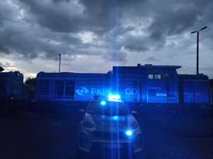 radiowóz stojący z włączonymi sygnałami świetlnymi przed pociągiem