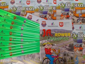 materiały edukacyjne w postaci kolorowych książeczek oraz zielone opaski odblaskowe