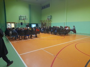 prelekcje na sali gimnastycznej w szkole, widoczna siedząca publiczność rodziców, przodem do niech stoi policyjny psycholog po cywilnemu