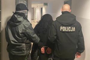 policjanci prowadzą przez korytarz komisariatu zatrzymaną kobietę z założonymi kajdankami na ręce trzymane z tyłu